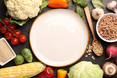 Photo of Healthy vegetarian food. Empty plate surrounded by different products on dark textured table, flat lay