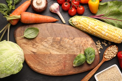 Photo of Healthy vegetarian food. Empty board surrounded by different products on dark textured table, flat lay