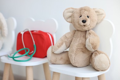 Photo of Pediatrician concept. Toy bear, medical bag and stethoscope on chairs in clinic