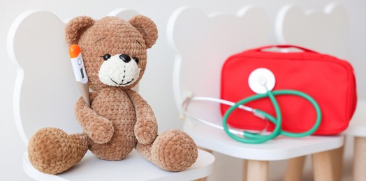 Photo of Pediatrician concept. Toy bear, thermometer, medical bag and stethoscope on chairs in clinic