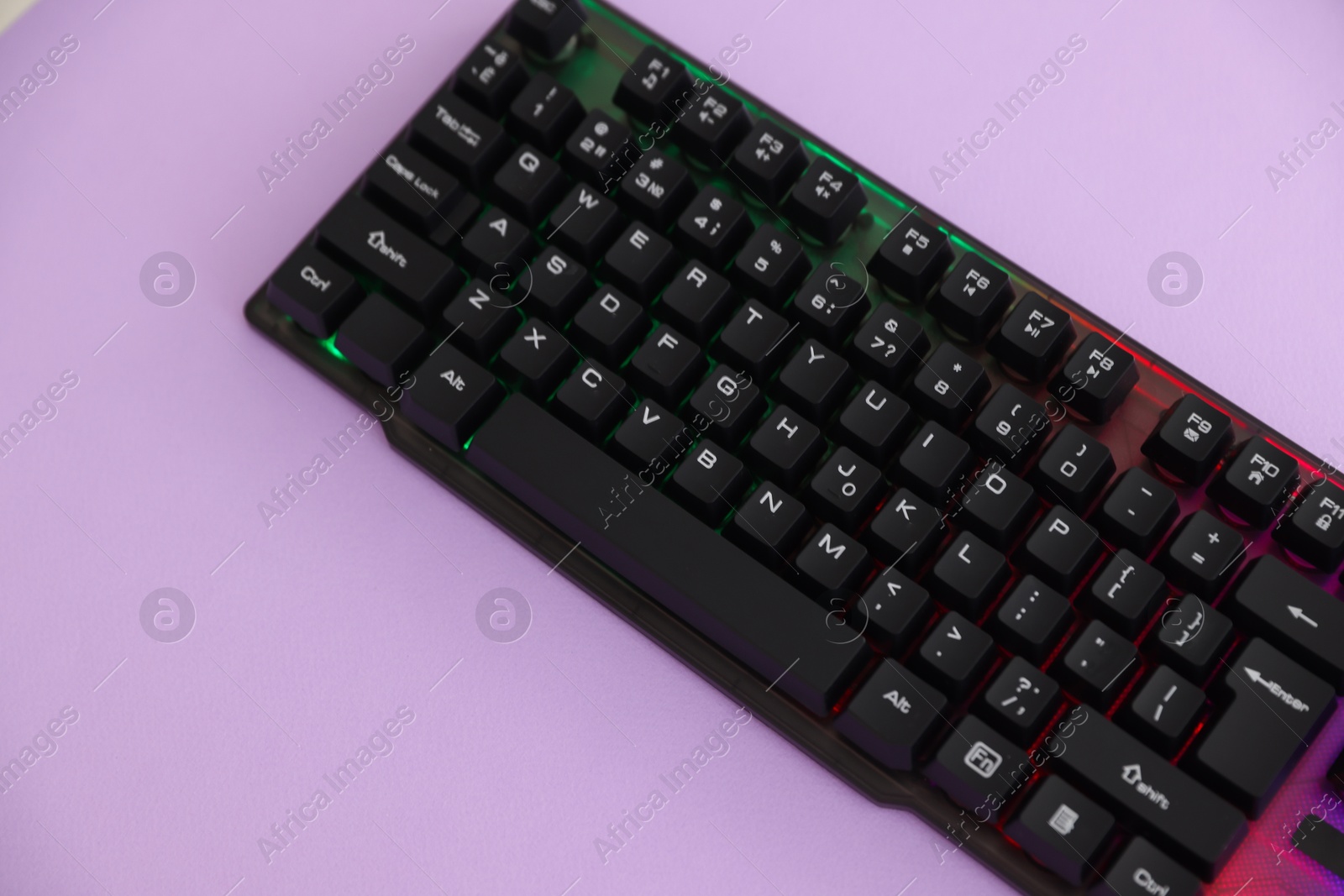 Modern computer keyboard with RGB lighting on violet background, above view. Space for text Photo of Modern computer keyboard with RGB lighting on violet background, above view. Space for text