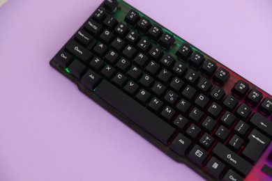 Photo of Modern computer keyboard with RGB lighting on violet background, above view. Space for text