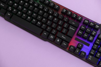Photo of Modern computer keyboard with RGB lighting on violet background, top view