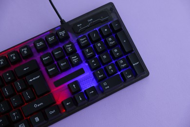 Photo of Modern computer keyboard with RGB lighting on violet background, top view. Space for text