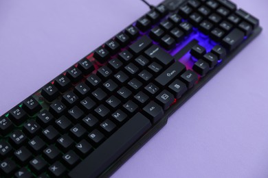 Photo of Modern computer keyboard with RGB lighting on violet background, closeup
