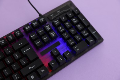 Photo of Modern computer keyboard with RGB lighting on violet background, above view