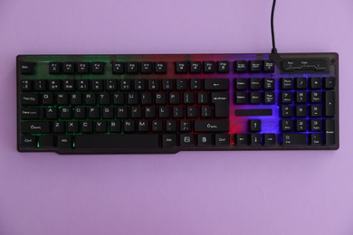 Photo of Modern computer keyboard with RGB lighting on violet background, top view