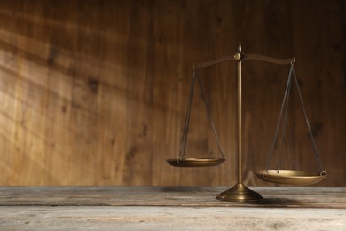 Photo of Golden scales of justice on wooden table. Space for text
