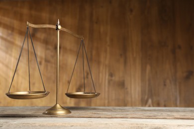 Photo of Golden scales of justice on wooden table. Space for text