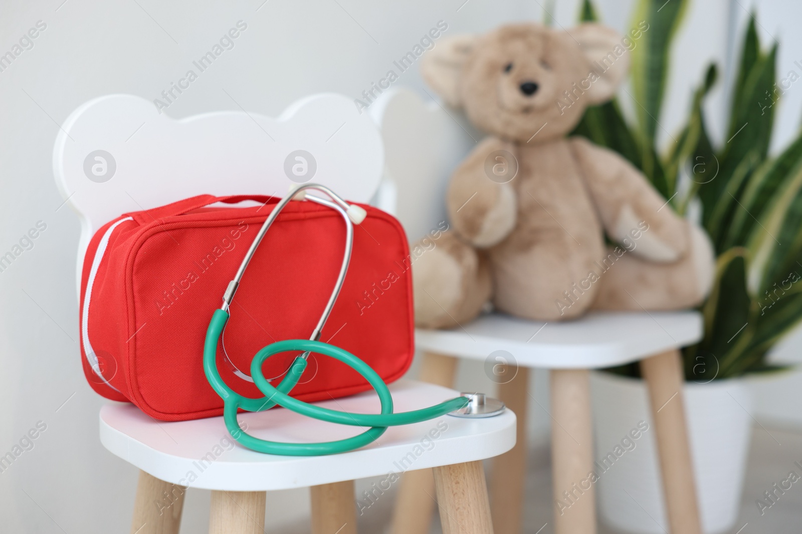 Photo of Pediatrician concept. Toy bear, medical bag and stethoscope on chairs in clinic, selective focus