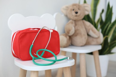 Photo of Pediatrician concept. Toy bear, medical bag and stethoscope on chairs in clinic, selective focus