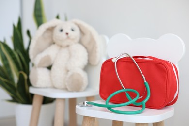 Photo of Pediatrician concept. Toy bunny, medical bag and stethoscope on chairs in clinic, selective focus