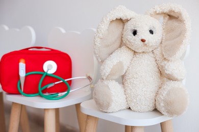Photo of Pediatrician concept. Toy bunny, medical bag and stethoscope on chairs in clinic