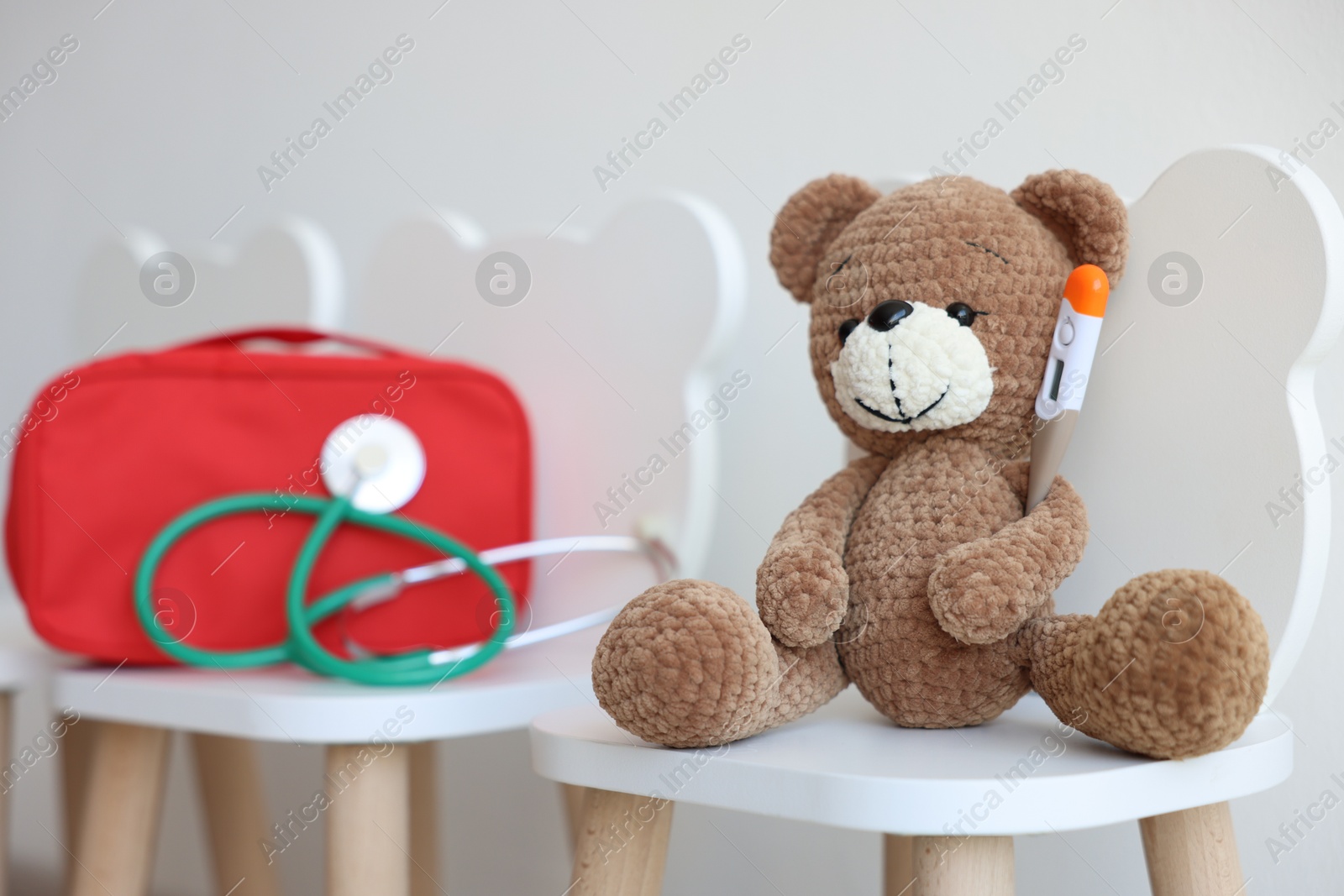 Photo of Pediatrician concept. Toy bear, thermometer, medical bag and stethoscope on chairs in clinic