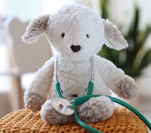 Photo of Pediatrician concept. Toy sheep and stethoscope on pouf in clinic, closeup