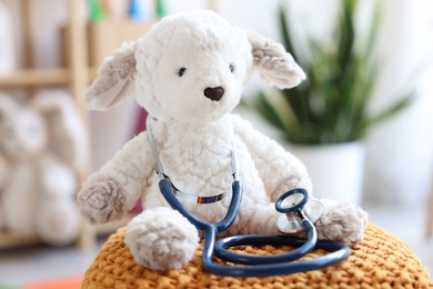 Photo of Pediatrician concept. Toy sheep and stethoscope on pouf in clinic, closeup
