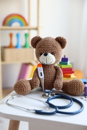 Photo of Pediatrician concept. Toy bear, thermometer and stethoscope on white table in clinic