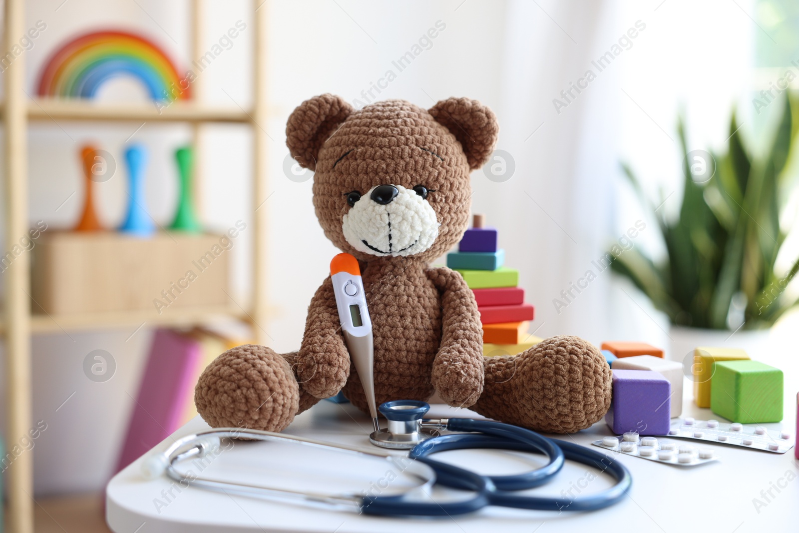 Photo of Pediatrician concept. Toy bear, thermometer and stethoscope on white table in clinic