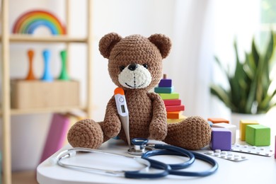 Photo of Pediatrician concept. Toy bear, thermometer and stethoscope on white table in clinic
