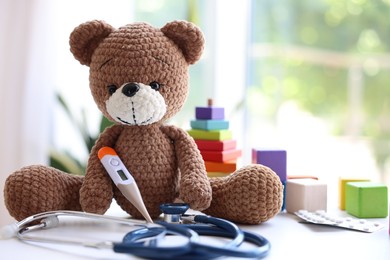 Photo of Pediatrician concept. Toy bear, thermometer and stethoscope on white table in clinic, closeup. Space for text