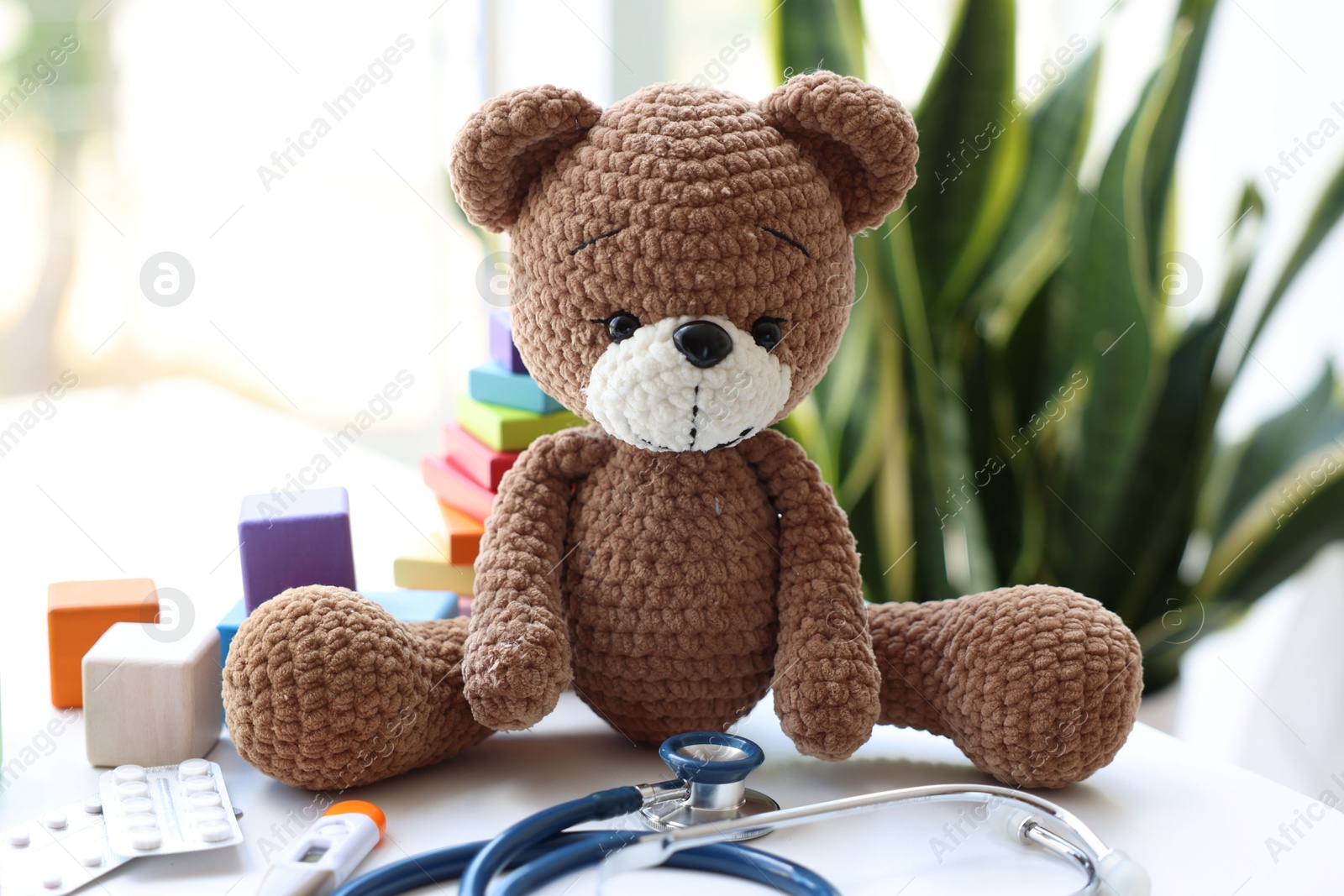 Photo of Pediatrician concept. Toy bear, thermometer and stethoscope on white table in clinic