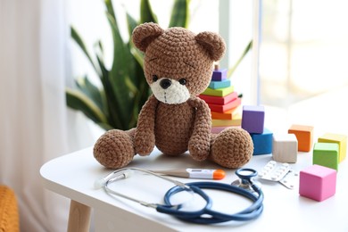 Photo of Pediatrician concept. Toy bear, thermometer and stethoscope on white table in clinic