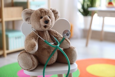 Photo of Pediatrician concept. Toy bear and stethoscope on chair in clinic, closeup. Space for text