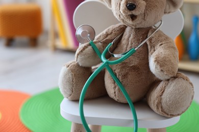 Photo of Pediatrician concept. Toy bear and stethoscope on chair in clinic, closeup