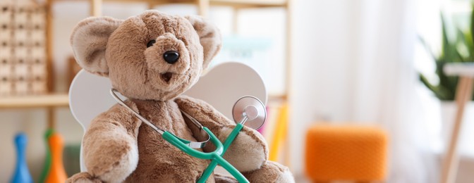Photo of Pediatrician concept. Toy bear and stethoscope on chair in clinic, closeup. Space for text