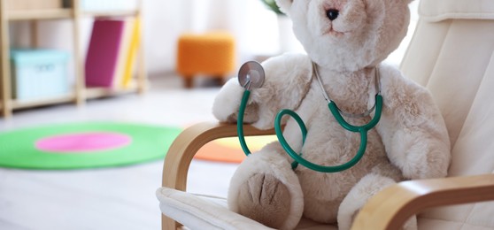 Photo of Pediatrician concept. Toy bear and stethoscope on armchair in clinic, closeup. Space for text