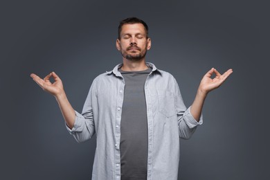 Photo of Panic attack. Man meditating to calm down on grey background