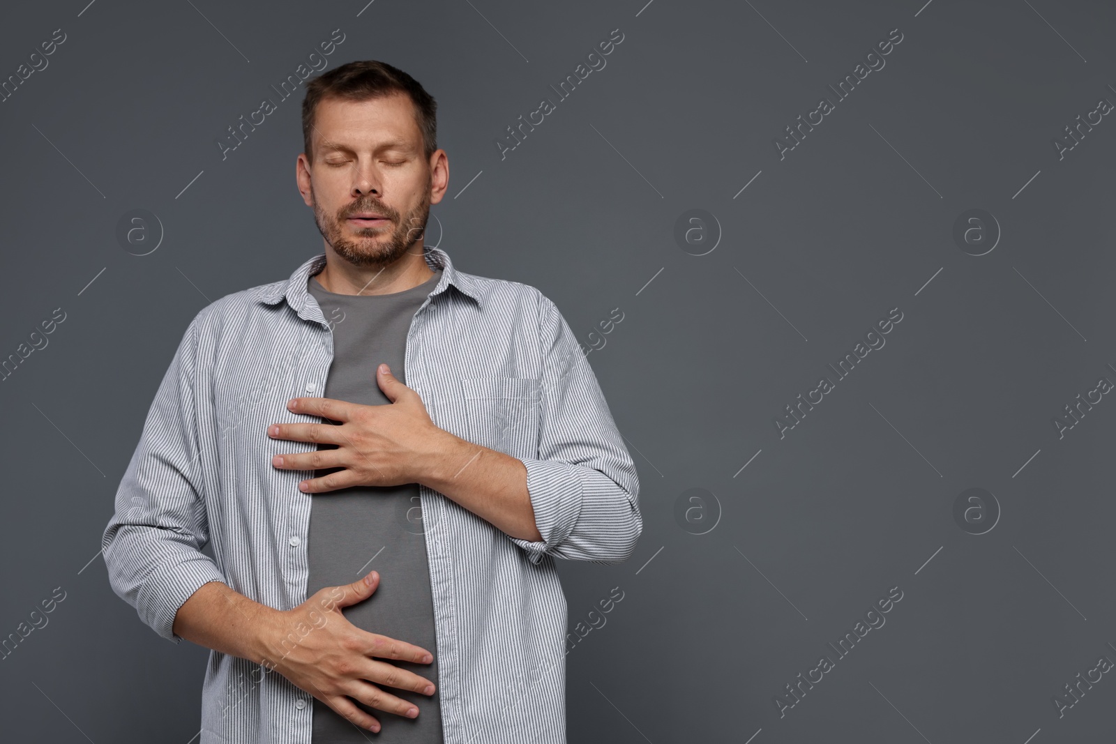 Photo of Panic attack. Man breathing to calm down on grey background, space for text