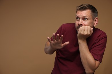 Photo of Man suffering from panic attack on brown background, space for text