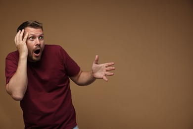 Photo of Man suffering from panic attack on brown background, space for text