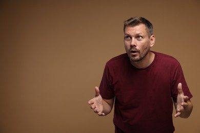 Photo of Man suffering from panic attack on brown background, space for text
