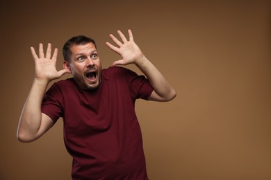 Photo of Man suffering from panic attack on brown background, space for text