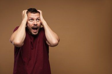 Photo of Man suffering from panic attack on brown background, space for text