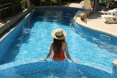 Photo of Girl with straw hat in swimming pool outdoors, back view