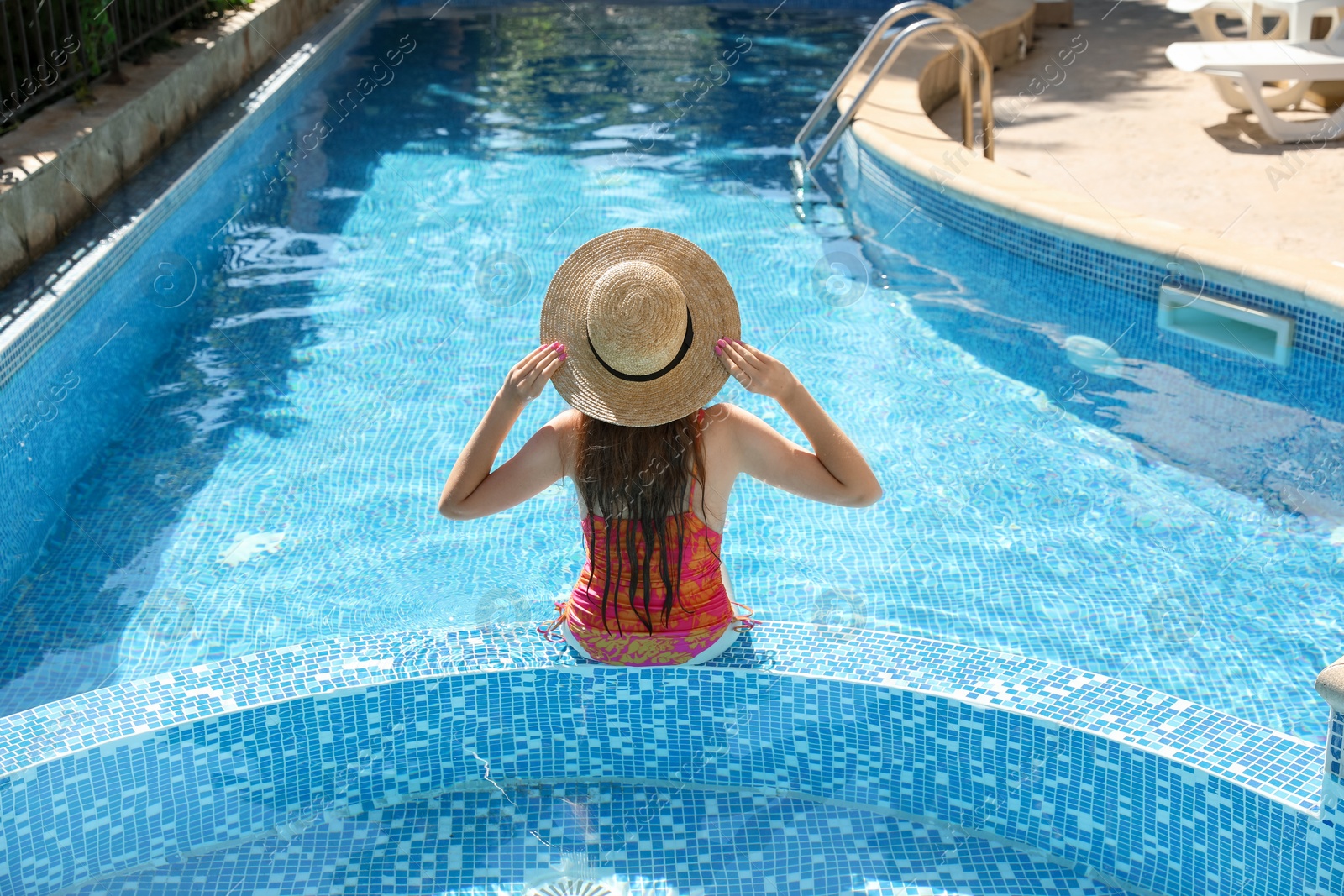 Photo of Girl with straw hat in swimming pool outdoors, back view