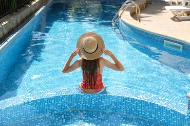 Photo of Girl with straw hat in swimming pool outdoors, back view