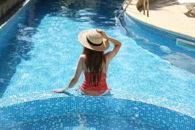 Photo of Girl with straw hat in swimming pool outdoors, back view