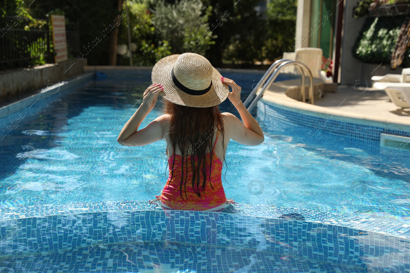 Photo of Girl with straw hat in swimming pool outdoors, back view