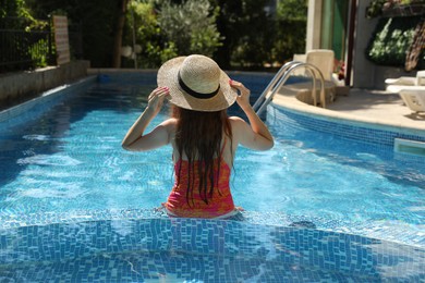 Photo of Girl with straw hat in swimming pool outdoors, back view