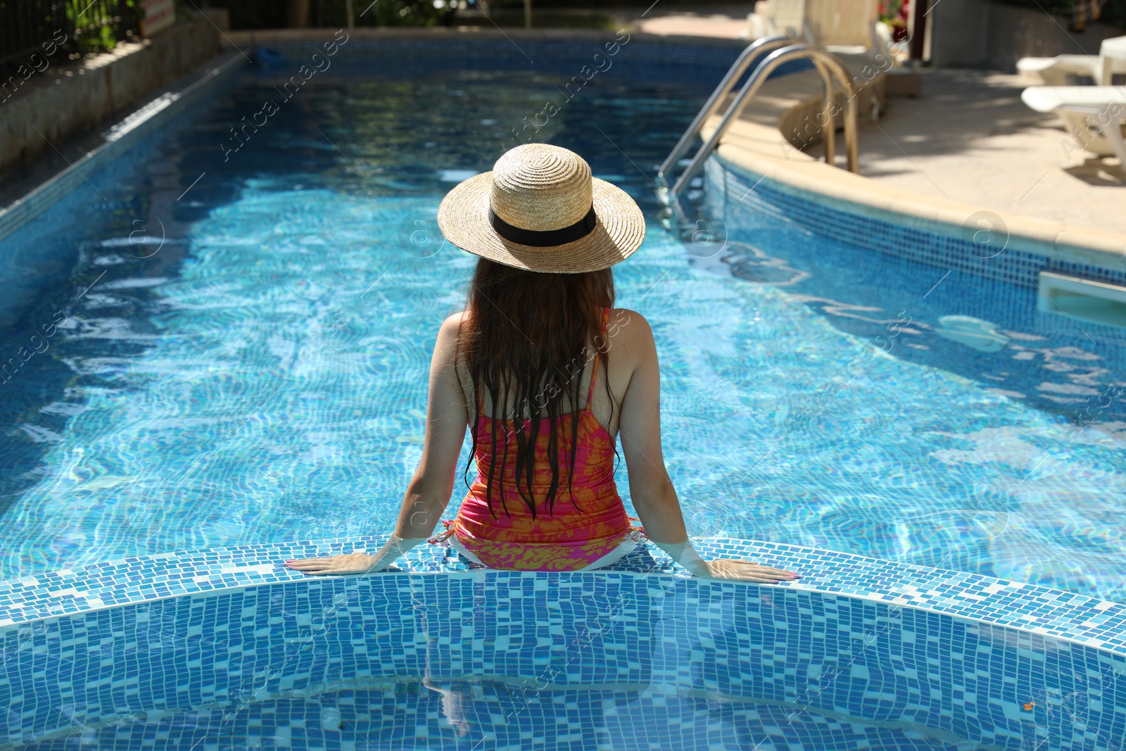 Photo of Girl with straw hat in swimming pool outdoors, back view
