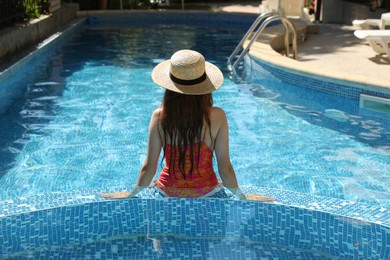 Photo of Girl with straw hat in swimming pool outdoors, back view