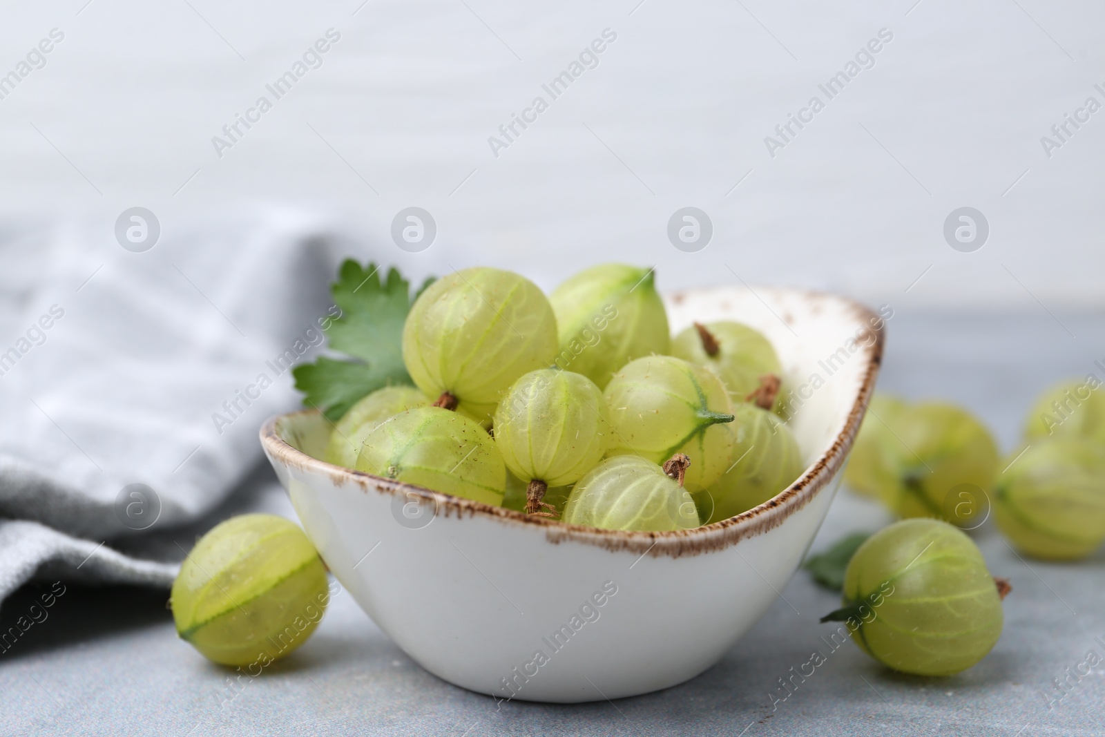 Photo of Fresh green gooseberries in bowl on grey table, closeup