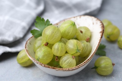 Photo of Fresh green gooseberries in bowl on grey table, closeup