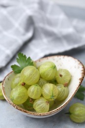 Photo of Fresh green gooseberries in bowl on grey table, closeup
