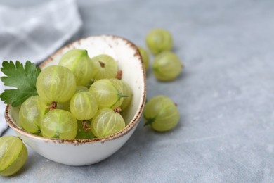 Photo of Fresh green gooseberries in bowl on grey table, closeup. Space for text