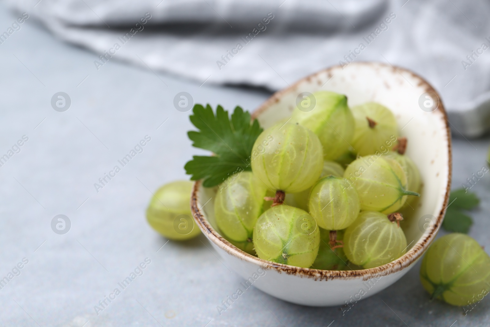 Photo of Fresh green gooseberries in bowl on grey table, closeup. Space for text